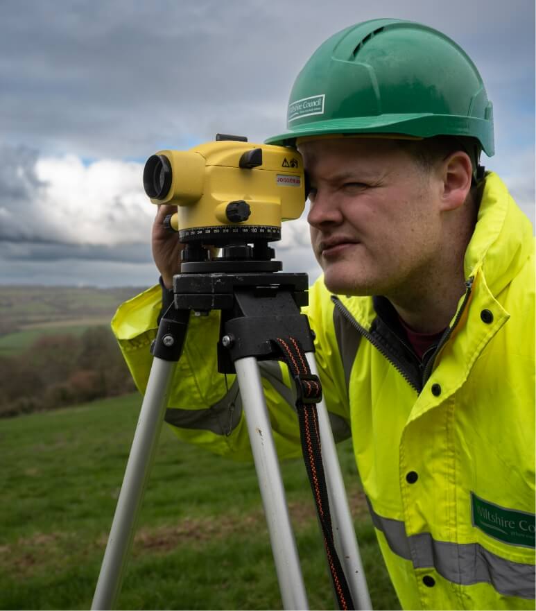 Person in hardhat and high vis jacket using surveying equipment in field