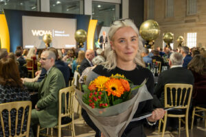 Lady smiling and holding flowers at an awards ceremony.